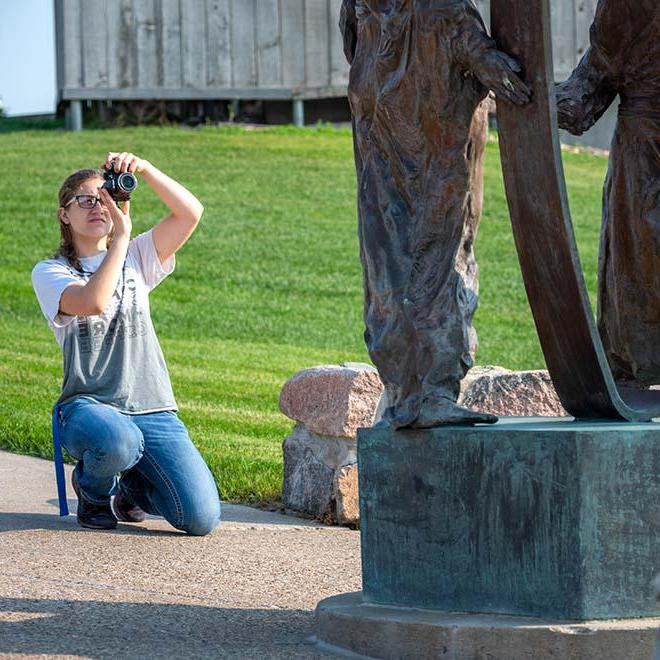 摄影专业的女学生在校园里给雕像拍照